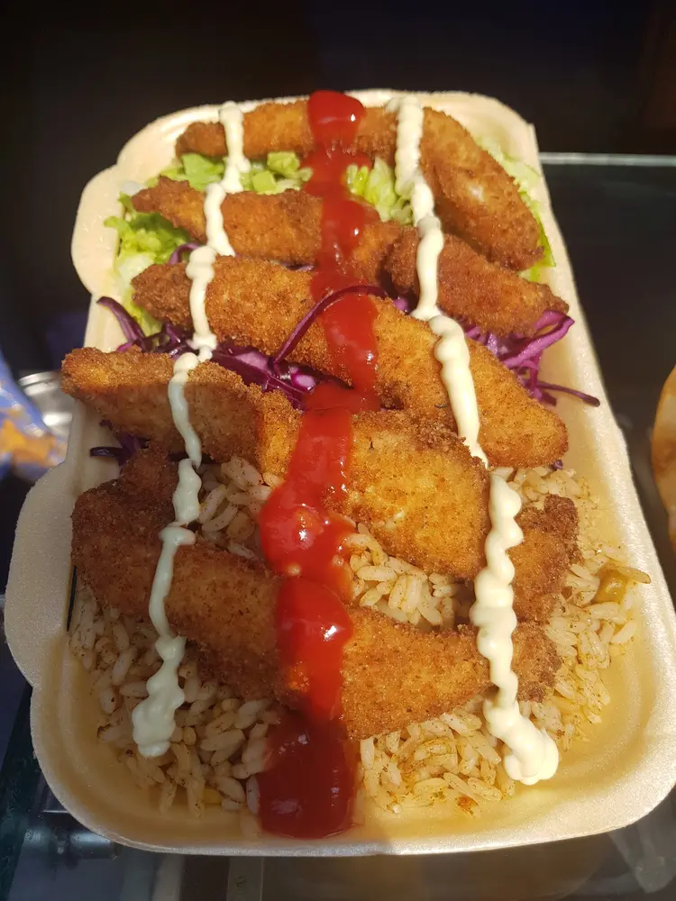 Takeaway box of breaded chicken goujons over seasoned rice with ketchup and mayo